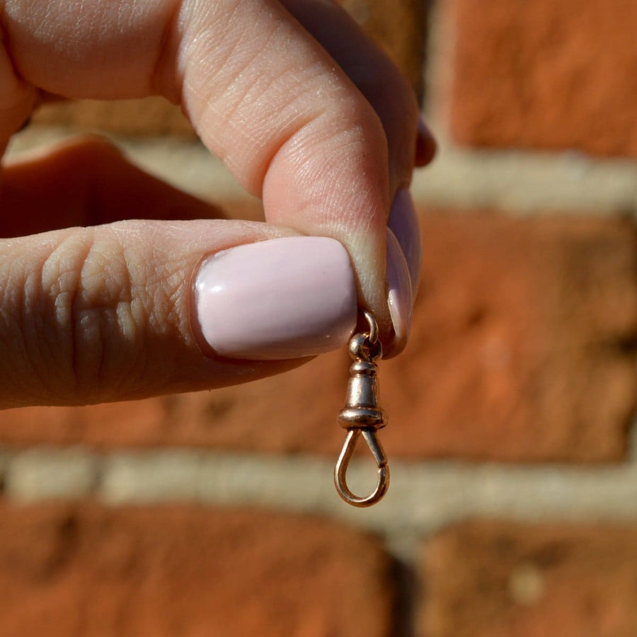 Close-up of a hand holding an Edwardian 9ct Gold Albert Dog Clip against a rustic brick background.