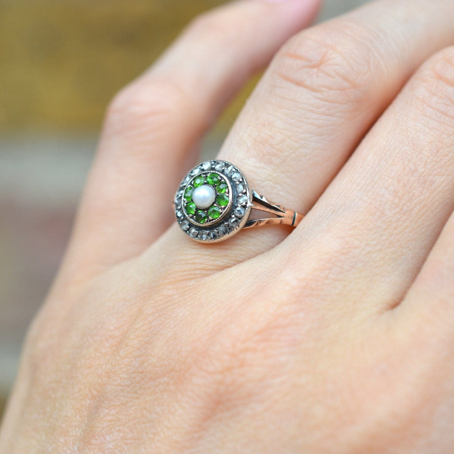 Edwardian 9ct gold target ring with green garnets, diamond halo, and central pearl worn on a hand.