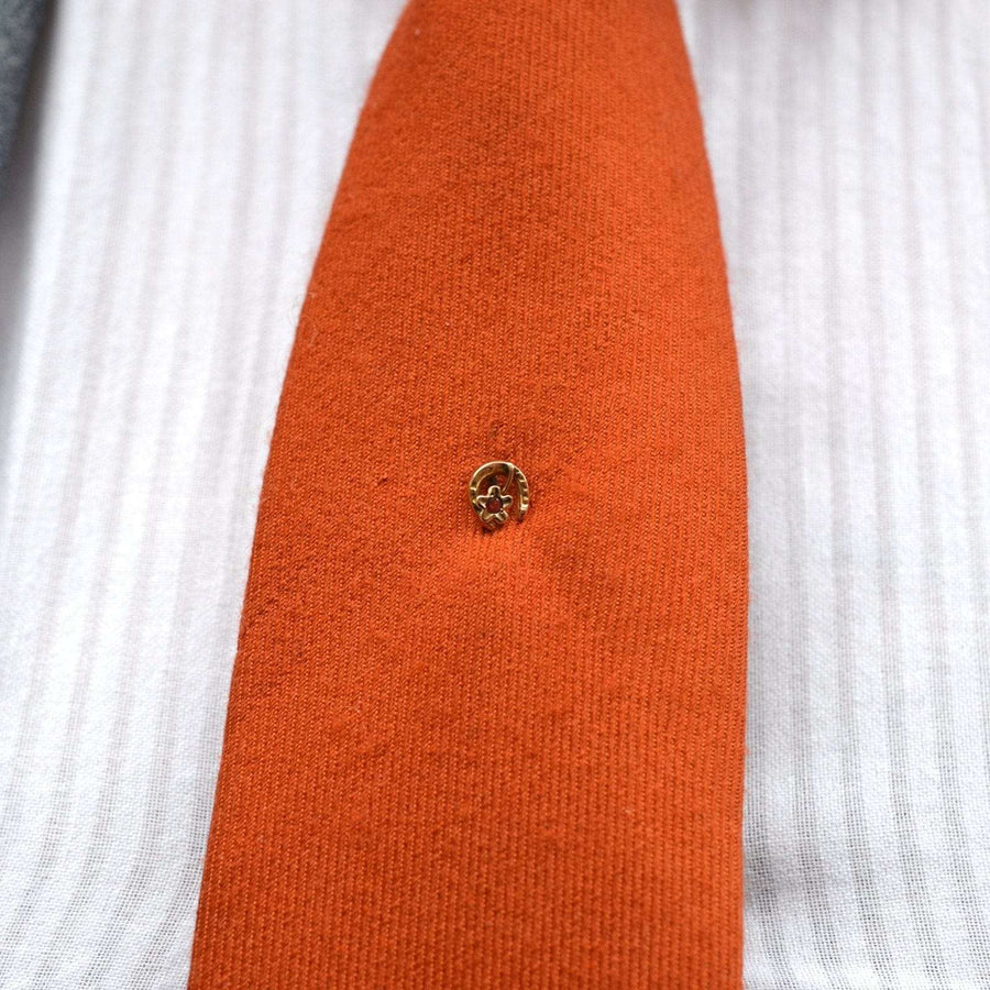 9ct gold horseshoe and flower garnet tie pin on orange tie, symbolizing good luck and protection.