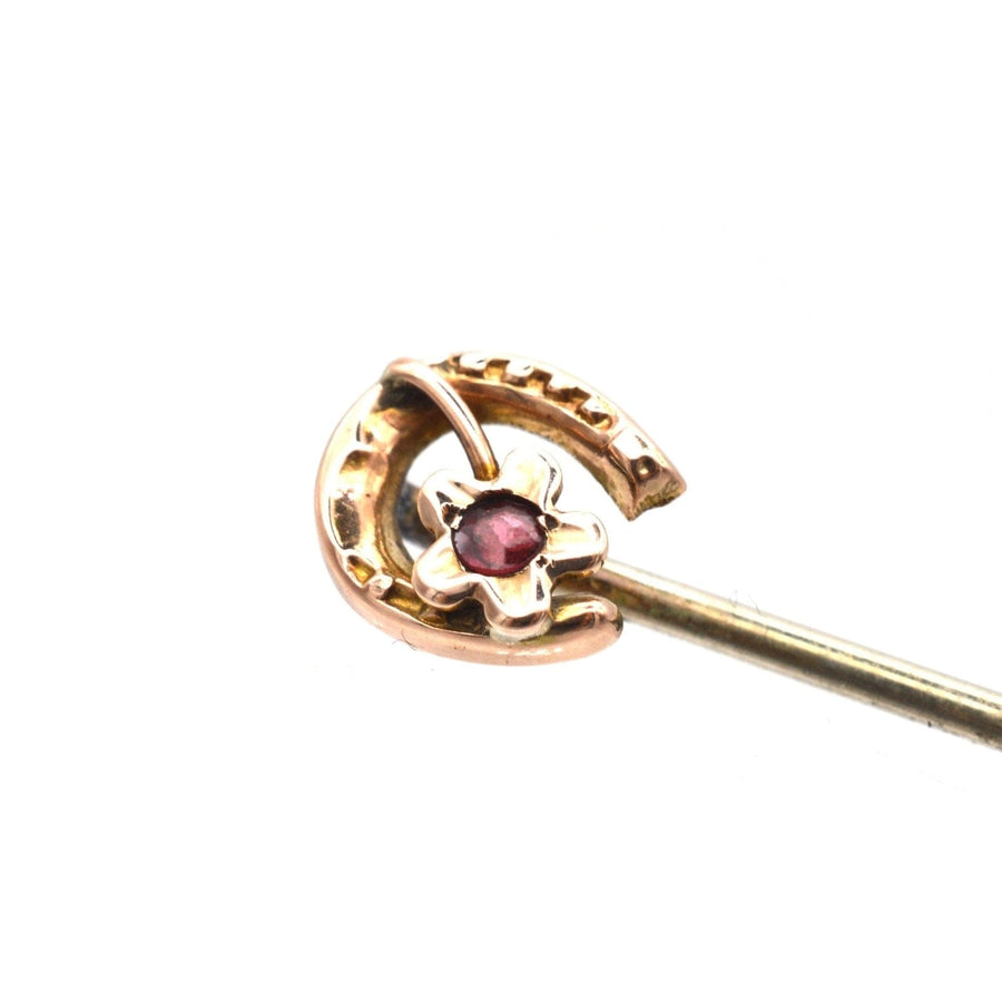 9ct gold horseshoe tie pin adorned with a garnet and floral accent, symbolizing luck and protection.