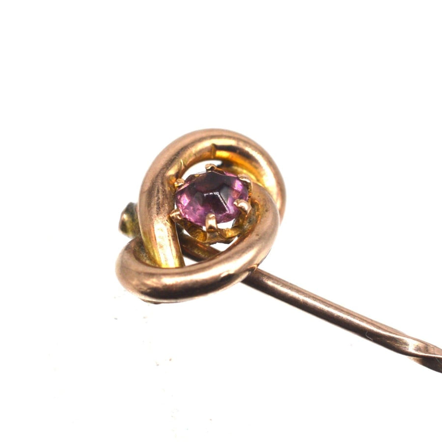 Edwardian 9ct gold lover's knot tie pin featuring a vibrant garnet centerpiece.