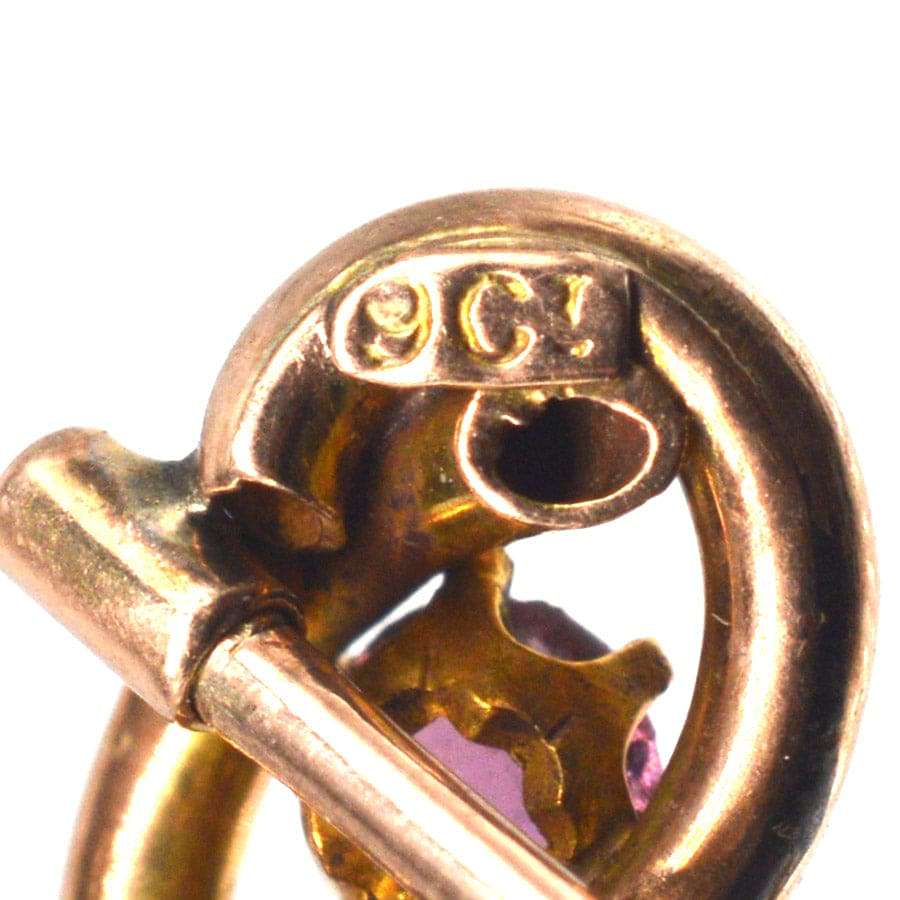 Close-up of Edwardian 9ct gold lover's knot tie pin showing hallmarks and vibrant garnet detail.