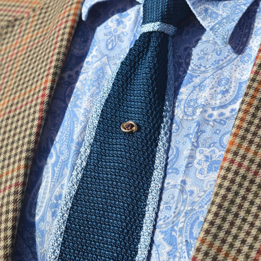 Edwardian 9ct gold lover's knot tie pin with garnet on a blue tie, styled with a checkered blazer.