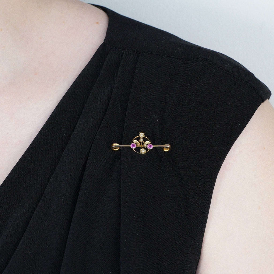 Edwardian 9ct gold brooch with pink sapphire and pearl flowers, elegantly displayed on a black dress.