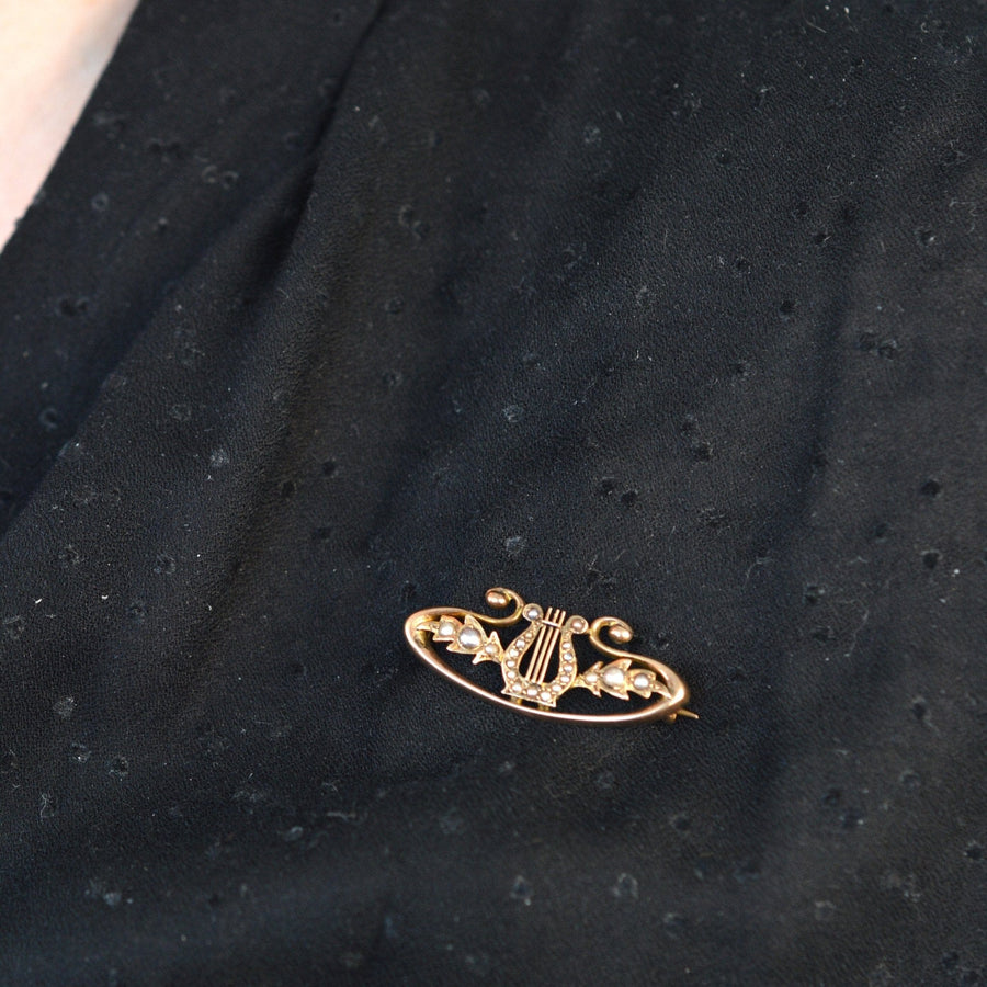 9ct gold bar brooch in lyre shape with split pearls, showcasing antique elegance on a black fabric.
