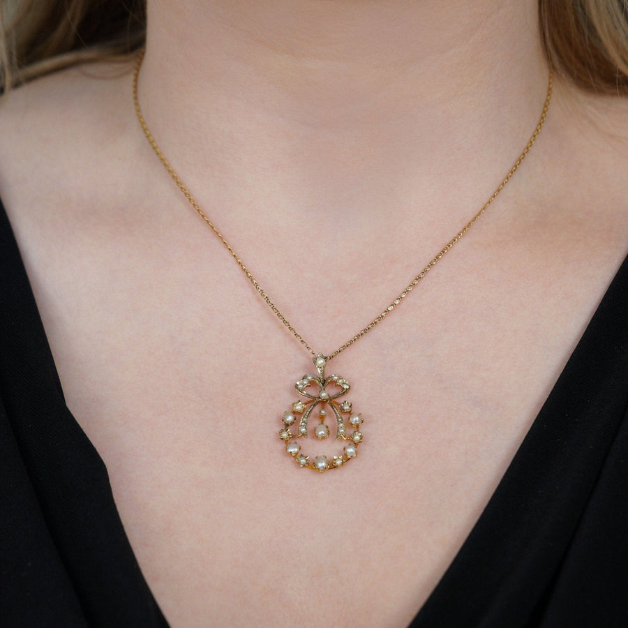 Edwardian 9ct gold pendant with split pearls and bow motif, featured on a model's neck.