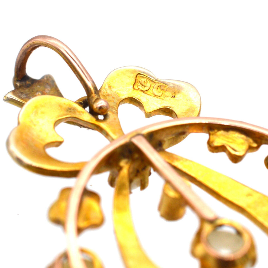 Close-up of Edwardian 9ct gold pendant featuring delicate bow motif and split pearls, highlighting intricate details.