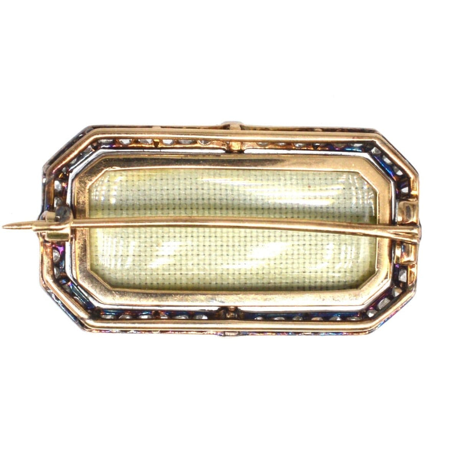 Antique brooch with intricate strapwork design in gold, featuring a greenish plaque and surrounded by decorative stones.