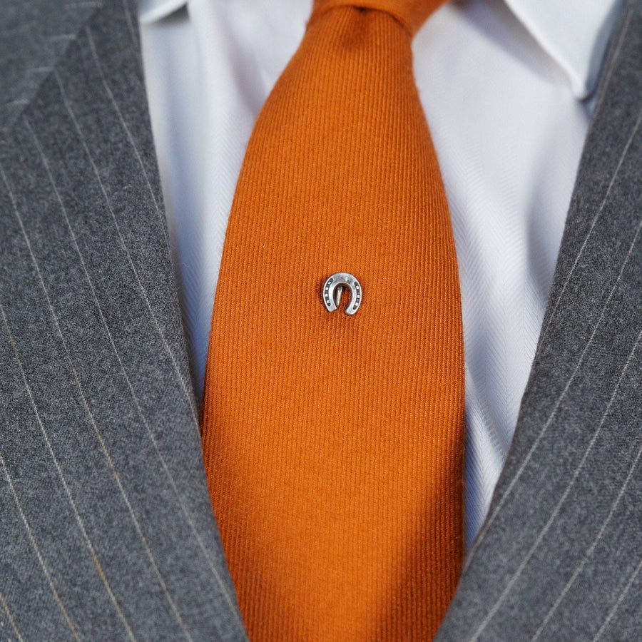 Edwardian silver lucky horseshoe tie pin on an orange tie, symbolizing good luck and protection.