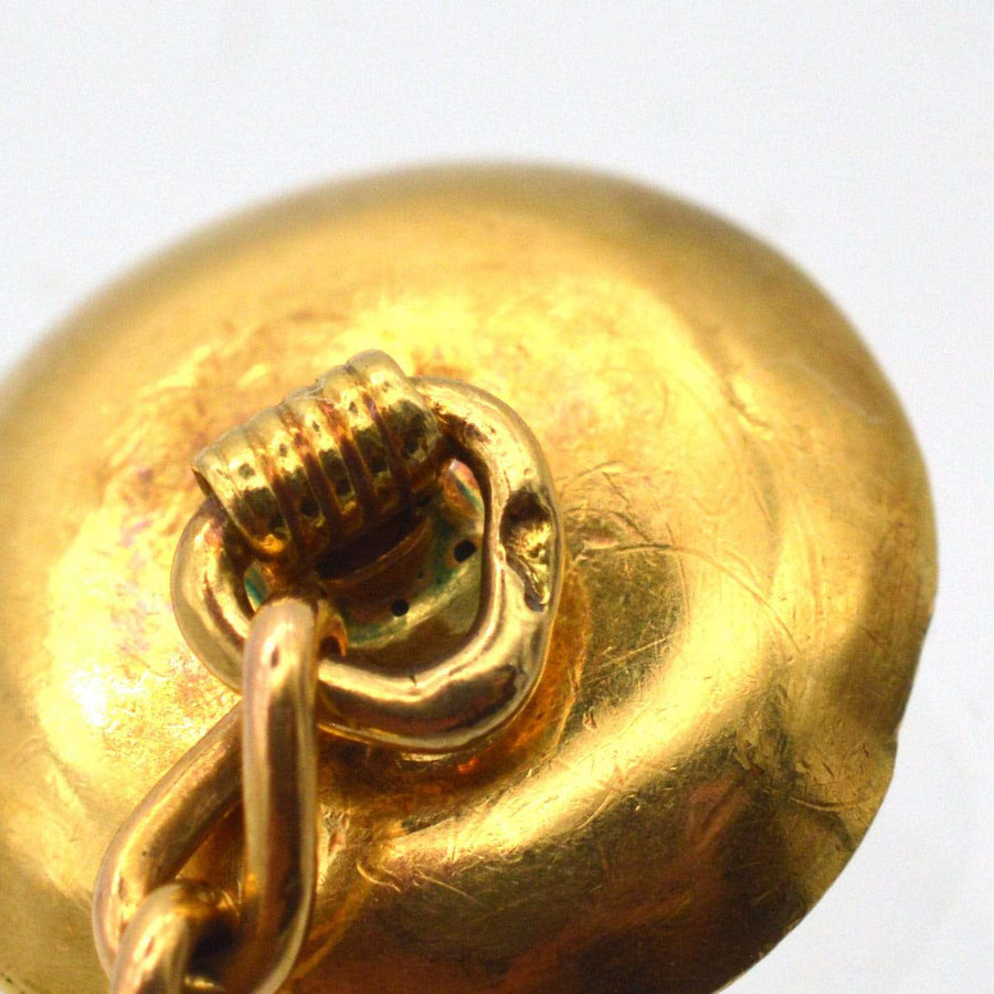 Close-up of a vintage gold cufflink with intricate detailing and attached chain, showcasing its craftsmanship.