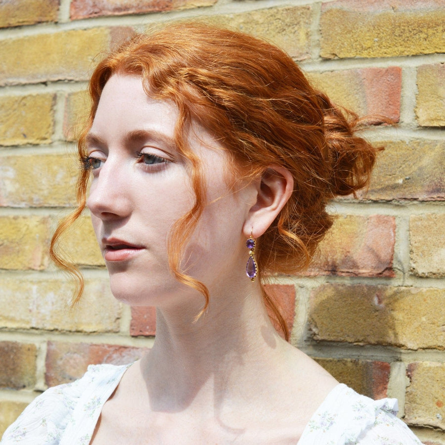 Model showcasing French 19th century gold earrings with amethyst and split pearl, against a brick wall.