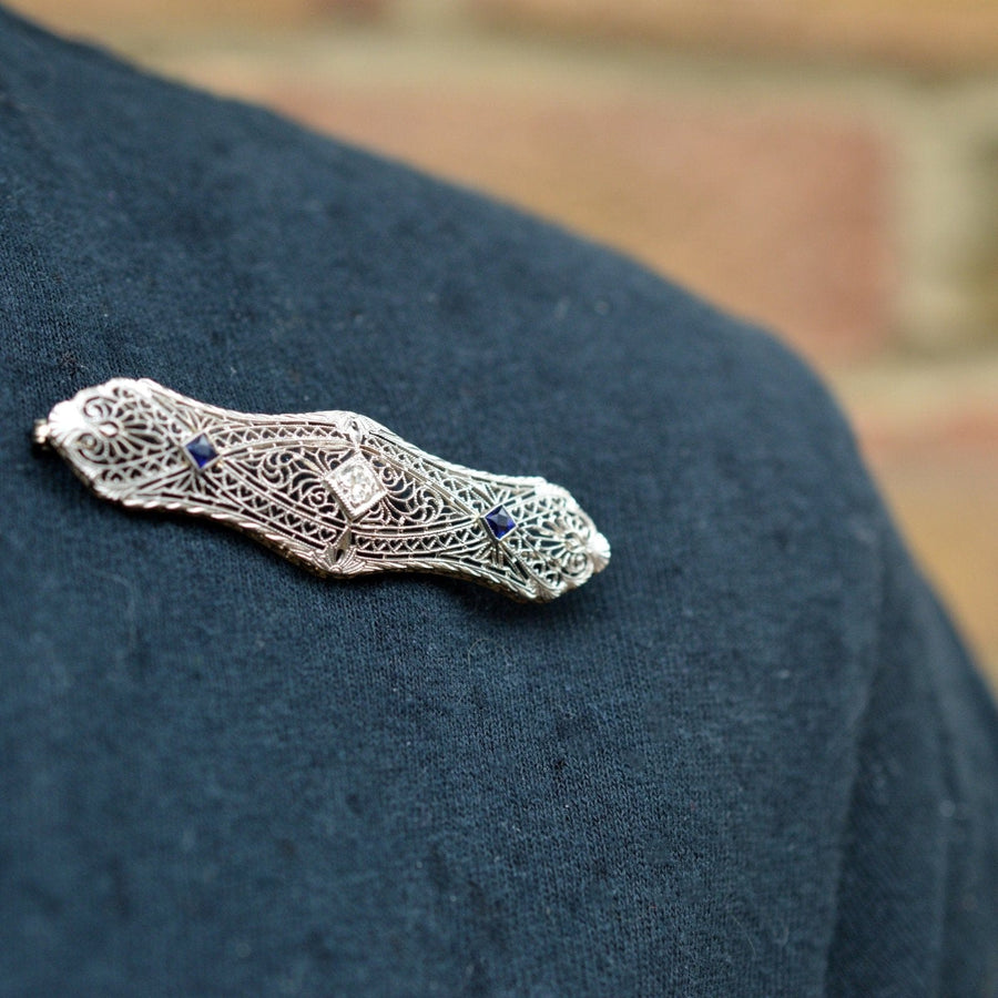 French Art Deco 14ct gold sapphire and diamond bar brooch on a dark fabric background.