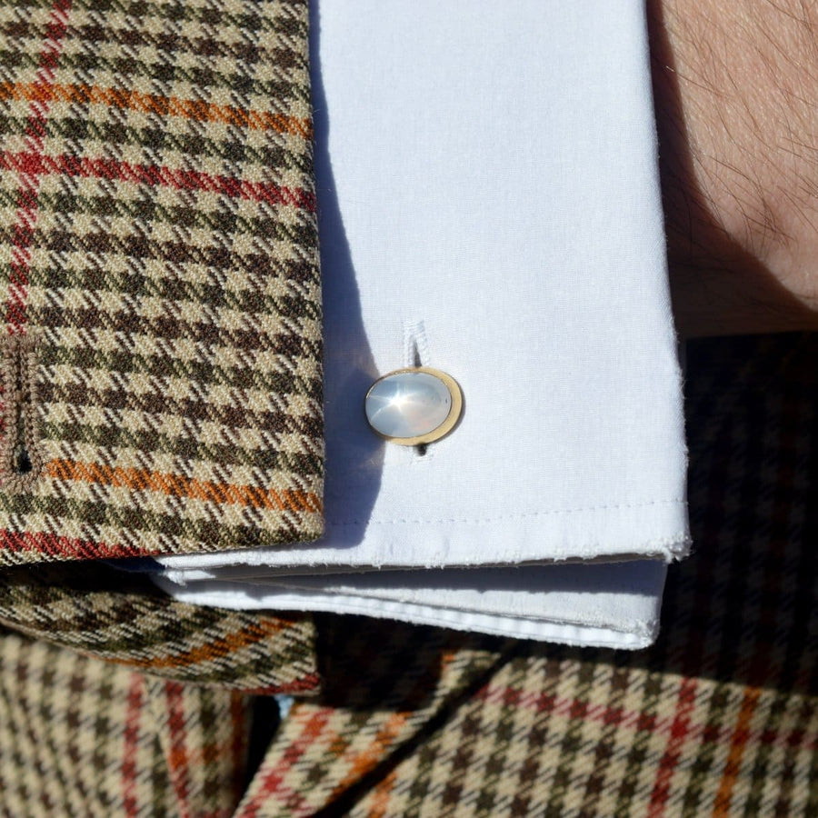 Elegant gold cufflinks with a moonstone, worn on a white shirt under a patterned blazer.