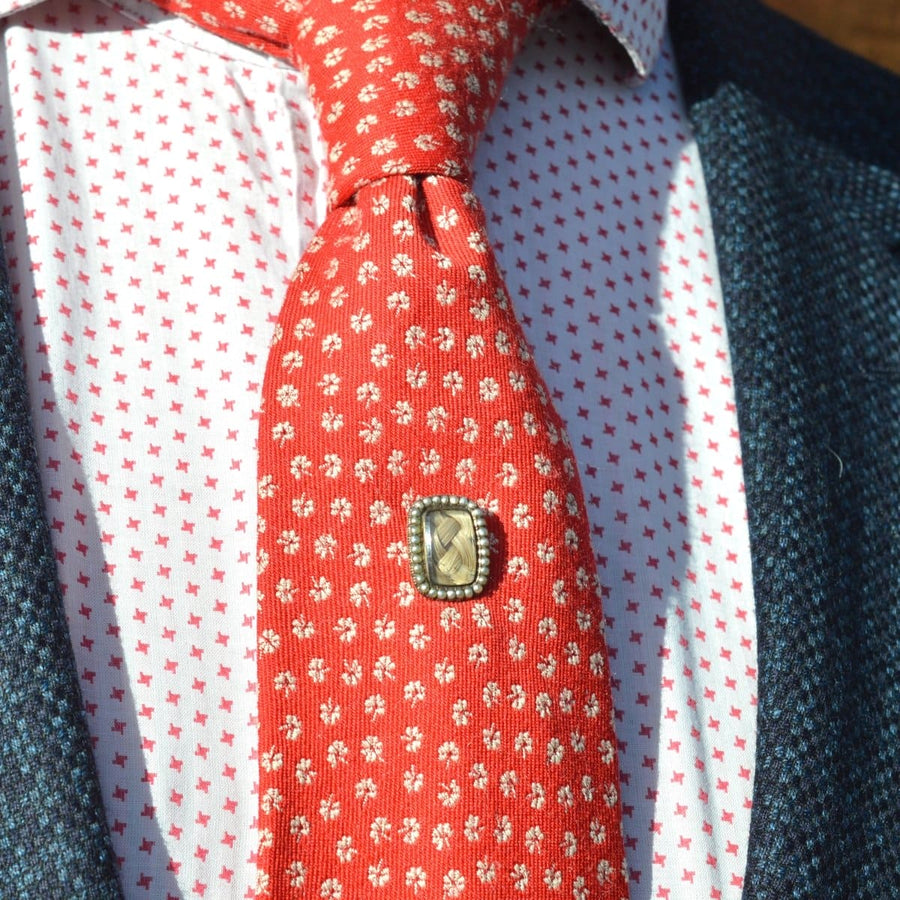 Georgian 9ct gold mourning tie pin on a red patterned tie, featuring a woven hair locket and seed pearls.