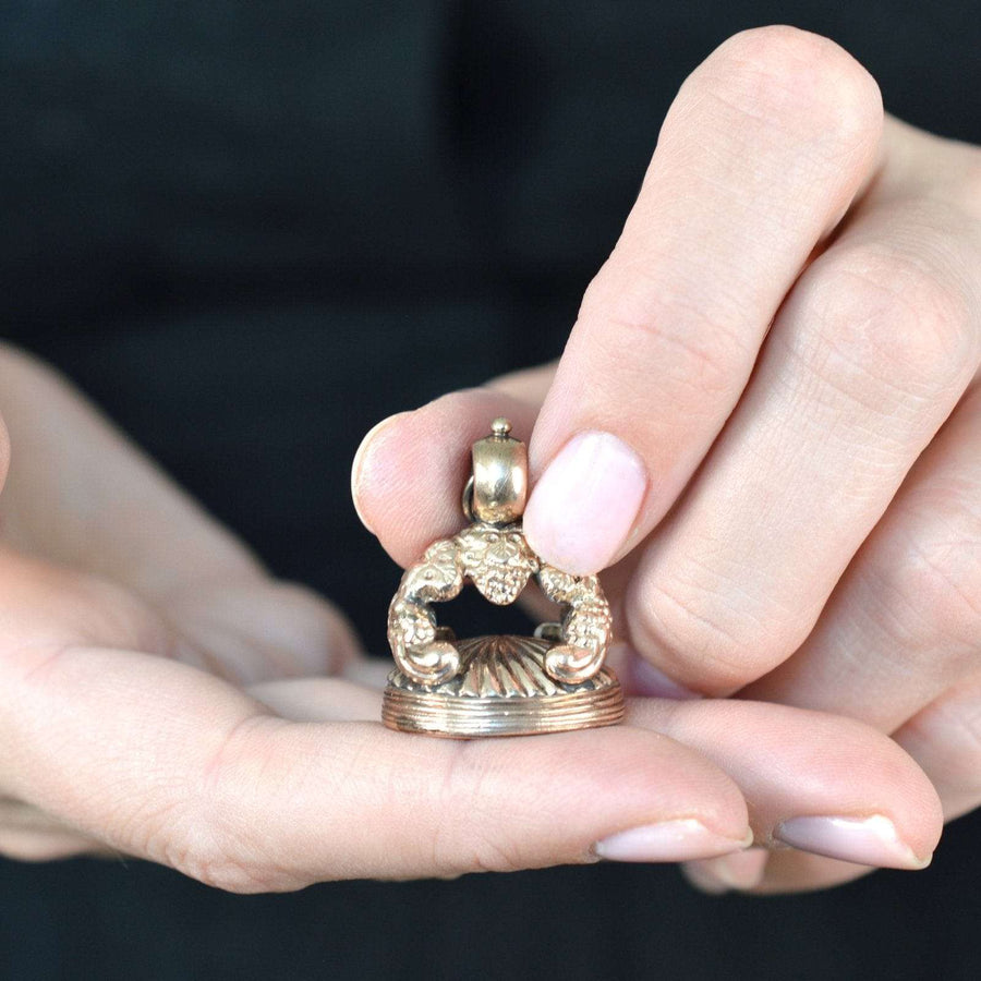 Close-up of a person holding a Georgian 9ct gold armorial seal with intricate design and crest detail.