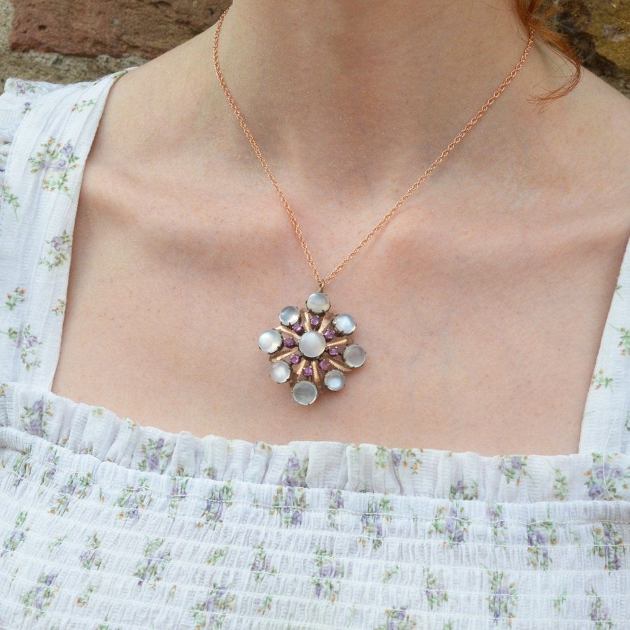 Large arts & crafts brooch pendant featuring moonstone and ruby, shown on a model in floral dress.