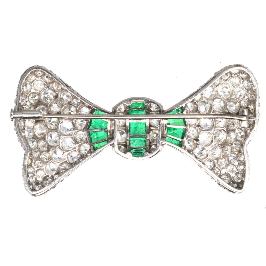 Large French Art Deco brooch featuring diamonds and emeralds in a bow design, set in platinum.