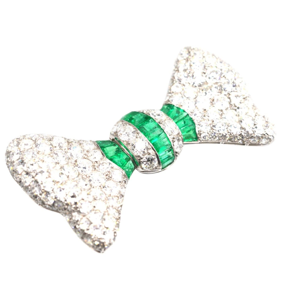 Art Deco platinum brooch featuring diamonds and emeralds in a bow shape, perfect for any stylish ensemble.