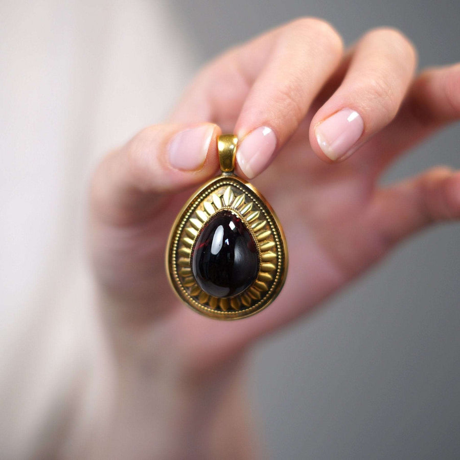 Large Victorian gold cabochon garnet pendant held in hand with intricate detailing.