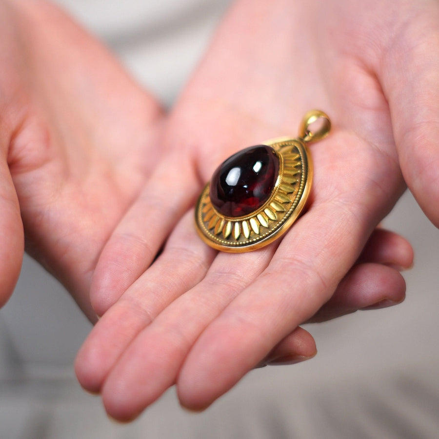 Large Victorian 15ct gold cabochon garnet pendant held in hands, showcasing intricate gold detailing.