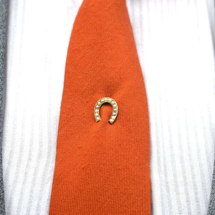 Large Victorian silver seed pearl horseshoe pin on orange tie, symbolizing good luck and protection from evil.