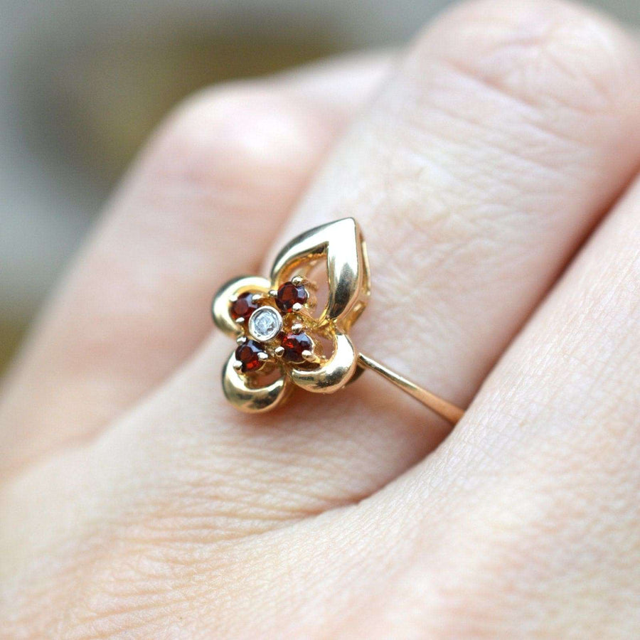 18ct gold ring featuring hessonite garnets and a diamond, shaped like a flower, worn on a finger.