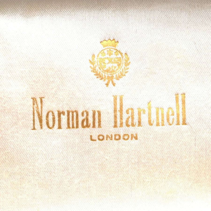 Norman Hartnell London logo in gold on a vintage fabric background, reflecting classic British design.