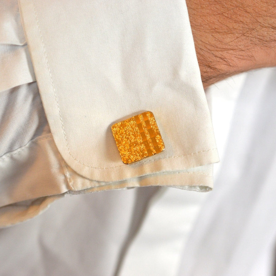 Close-up of a square yellow cufflink on a white dress shirt sleeve.