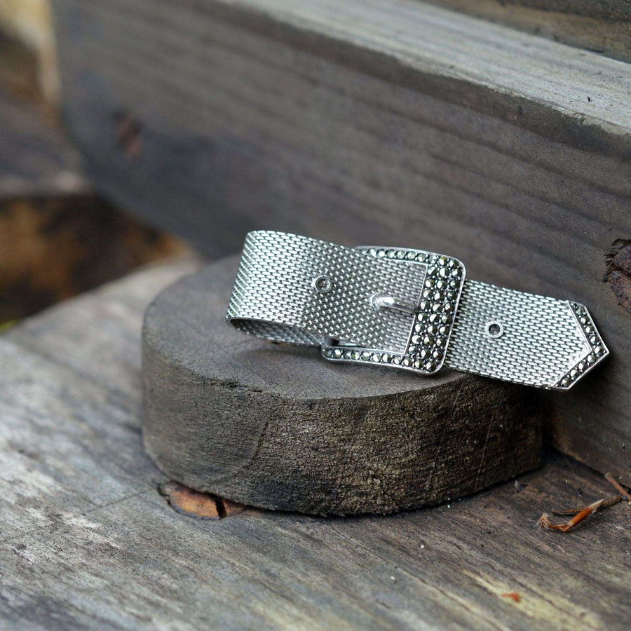Mid Century silver and marcasite buckle brooch displayed on a rustic wooden surface, showcasing timeless elegance.