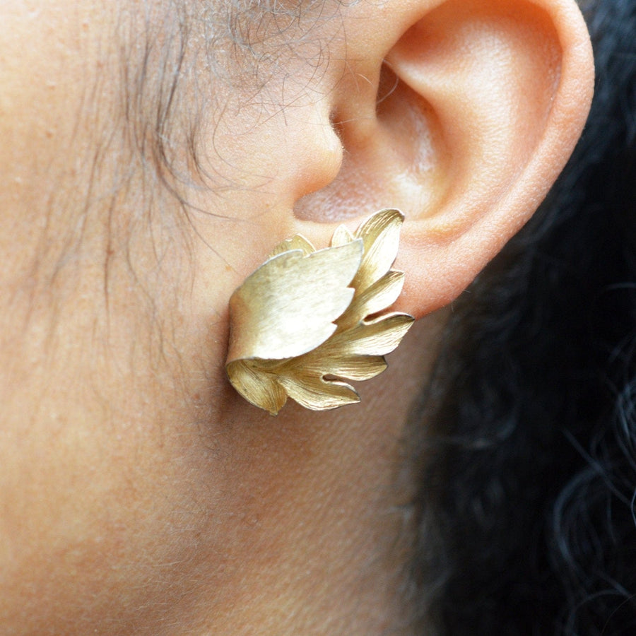Mid Century Trifari gilt metal leaf earrings displayed on a model's ear, showcasing the elegant baroque style.