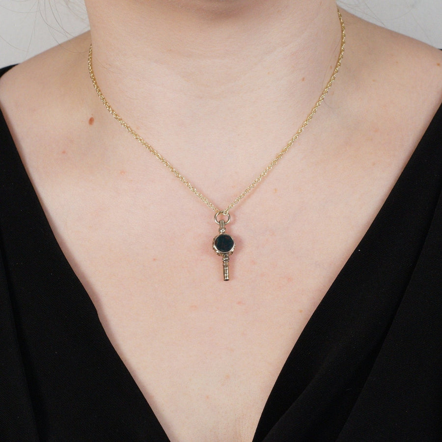 Gold cased watch key pendant featuring bloodstone and amethyst, worn as jewelry on a model's neck.