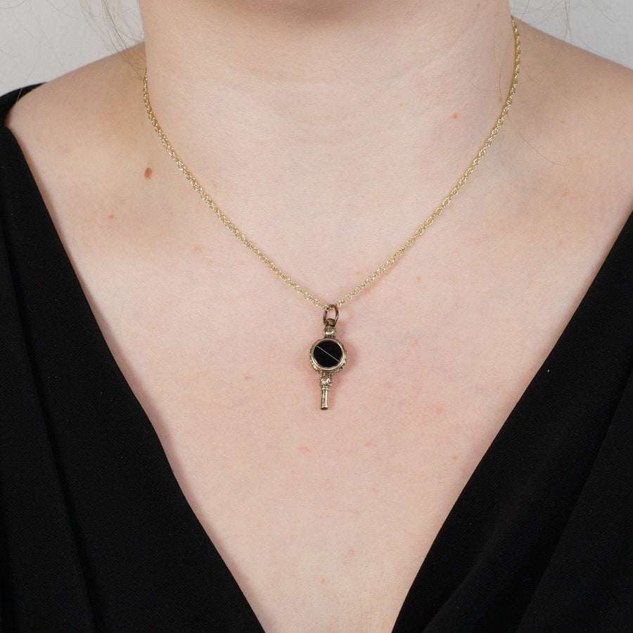 Gold cased watch key pendant with banded onyx on a delicate chain, showcasing antique elegance.
