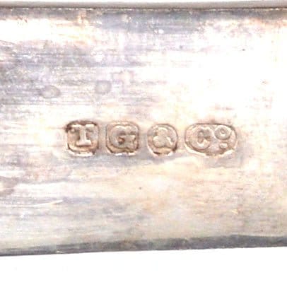 Close-up of hallmarks on silver cutlery stamped 'T.G.& Co.' showcasing fine craftsmanship and authenticity.