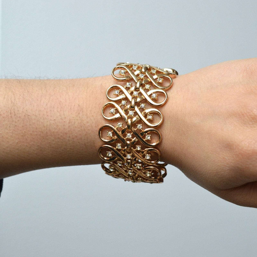 Trifari gold-tone vintage bracelet with interlinked swirls and diamond pastes on a wrist.