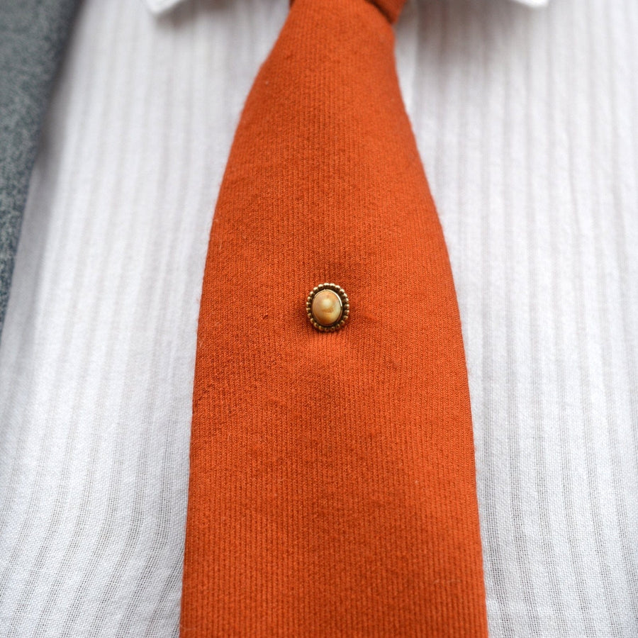 Victorian 9ct gold brown cat's eye shell tie pin on an orange tie, showcasing vintage elegance and unique design.