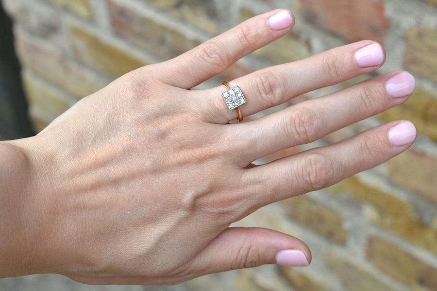 Vintage 18ct gold and platinum diamond square ring showcased on a hand with pink nails, set against a stone wall.