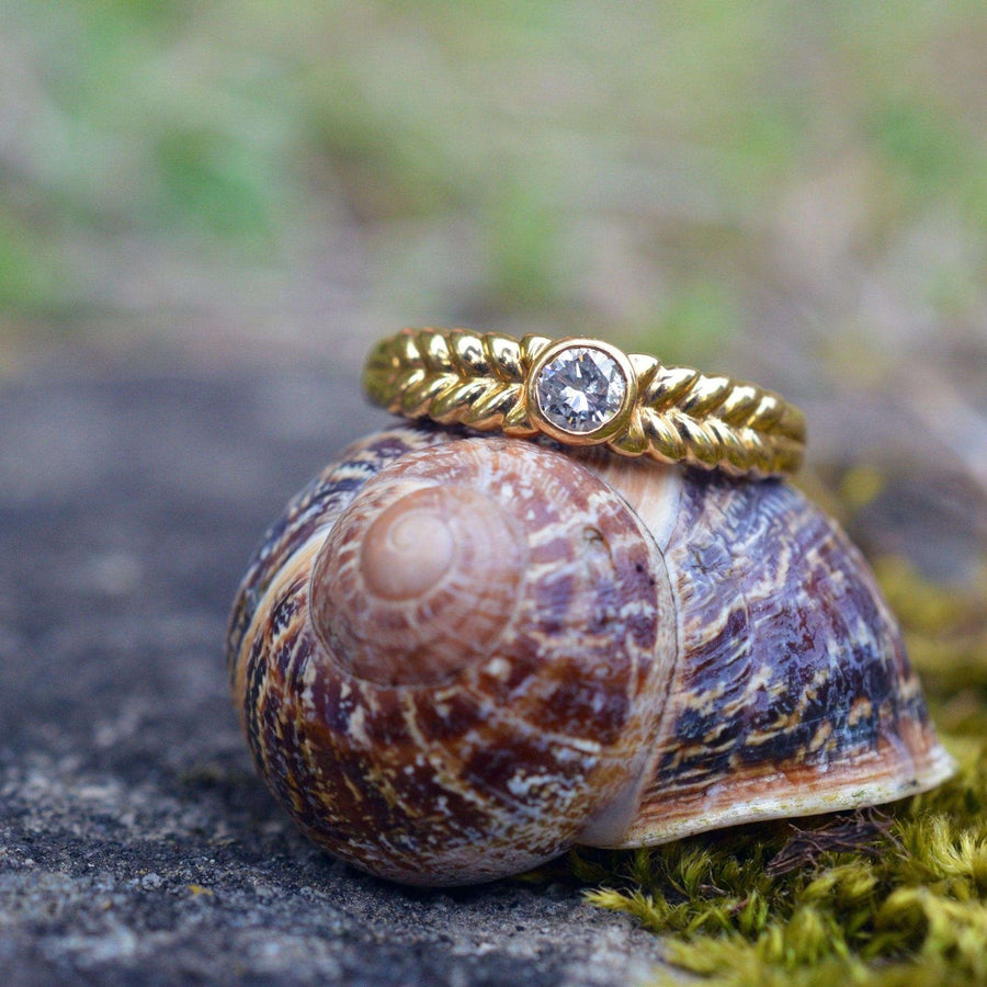 Vintage 18ct gold diamond solitaire ring displayed on a textured snail shell outdoors.