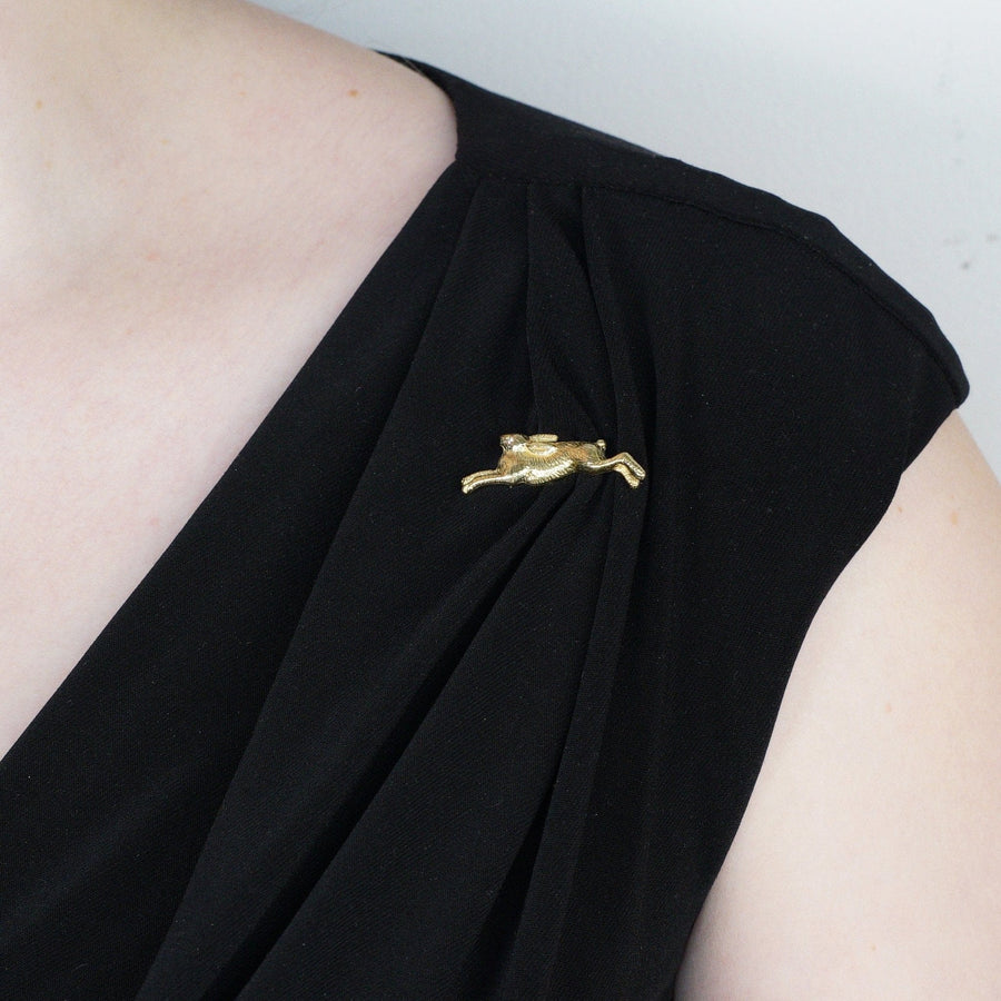 Vintage 18ct gold running rabbit brooch on a black dress, featuring a playful design with a golden finish.