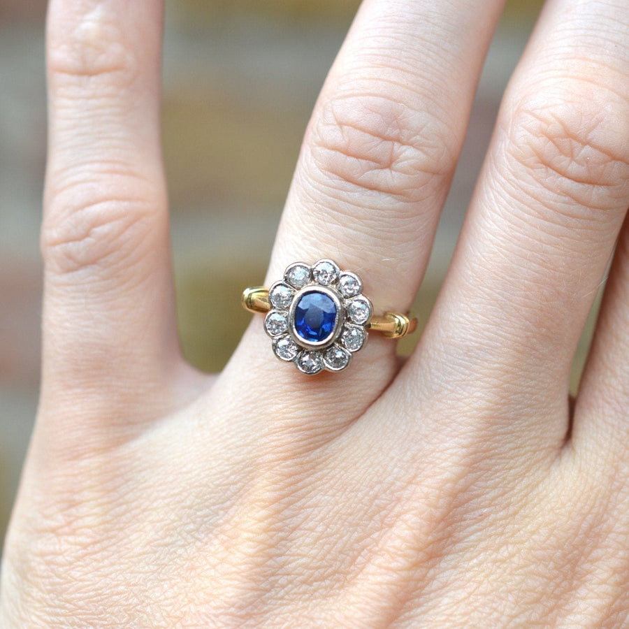 Vintage 18ct gold cluster ring featuring a blue sapphire and sparkling diamond halo on a hand.