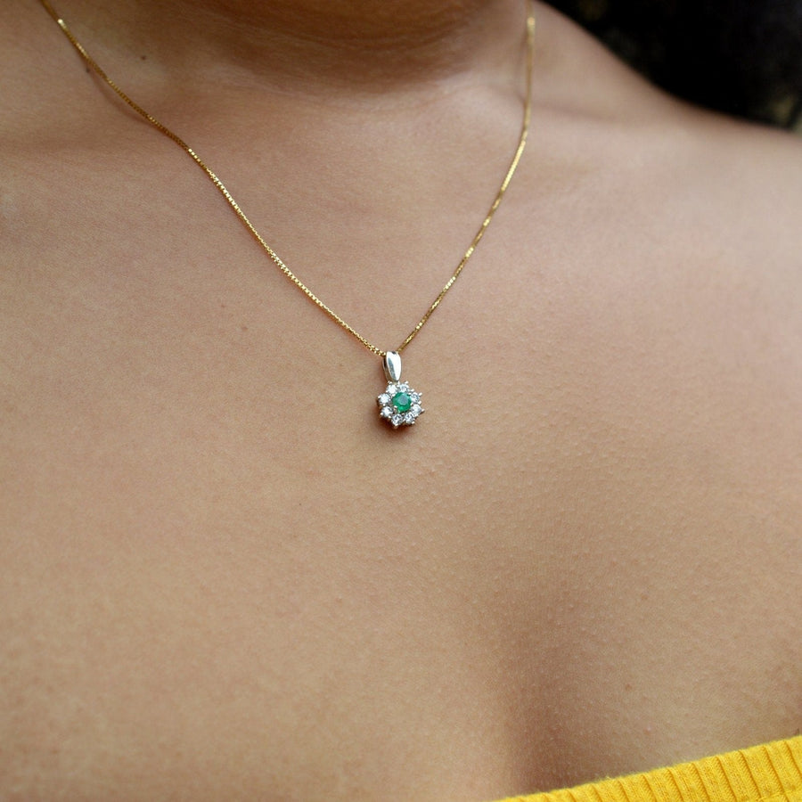 Vintage 18ct white gold emerald and diamond cluster pendant worn on a gold chain, highlighting its elegant design.