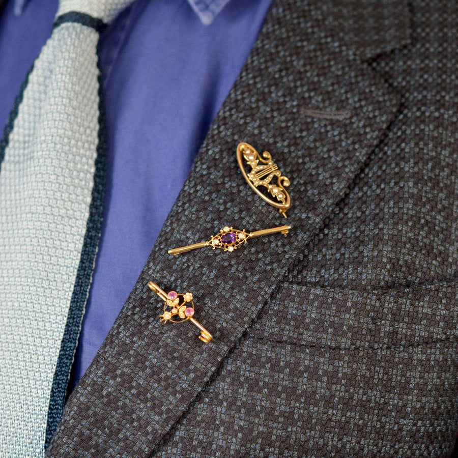Close-up of three vintage gold brooches with amethyst and diamonds on a suit lapel.