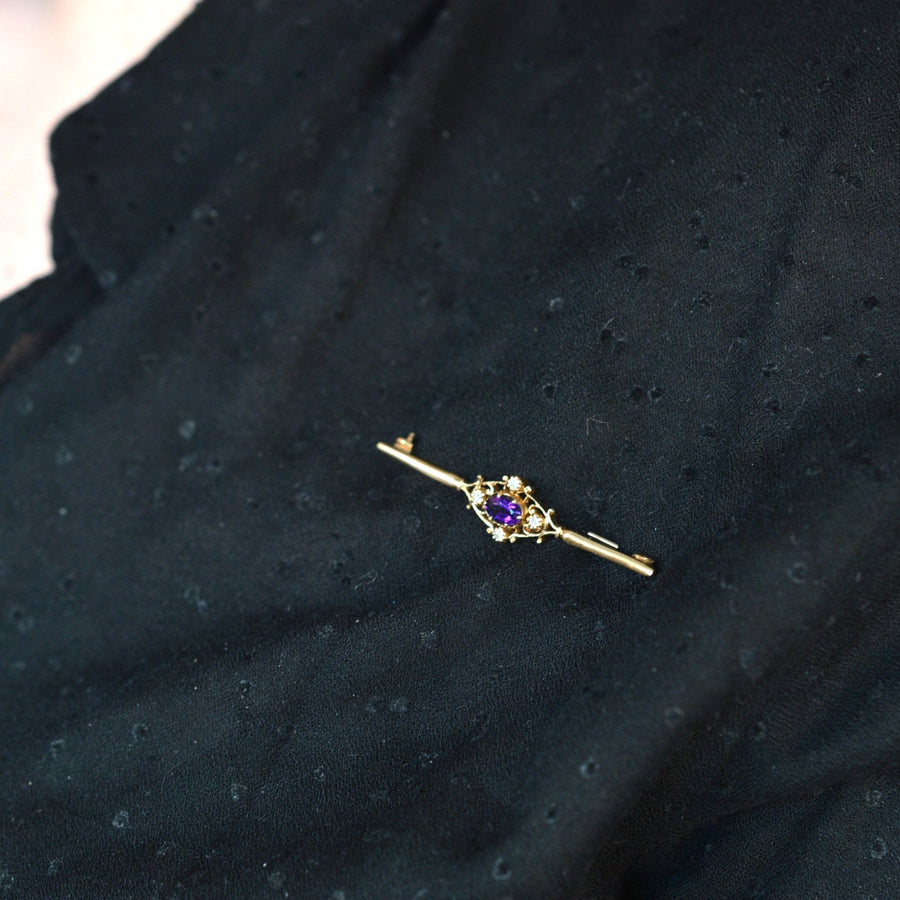 Vintage 9ct gold bar brooch featuring an amethyst and diamond centerpiece on a textured black fabric.