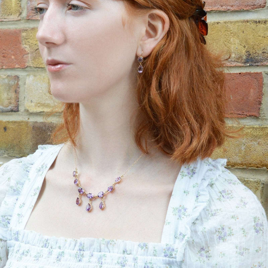 Model showcases vintage 9ct gold amethyst drop earrings against a brick background.