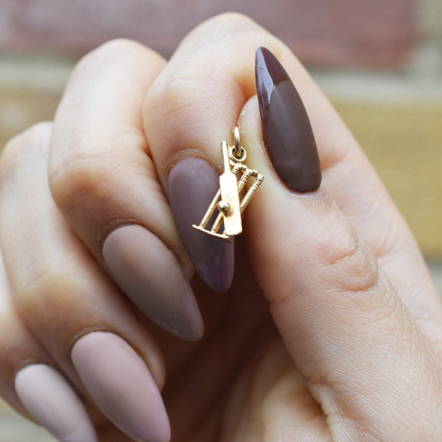 9ct gold cricket bat, ball and stumps charm pendant held between fingers, perfect for cricket fans.