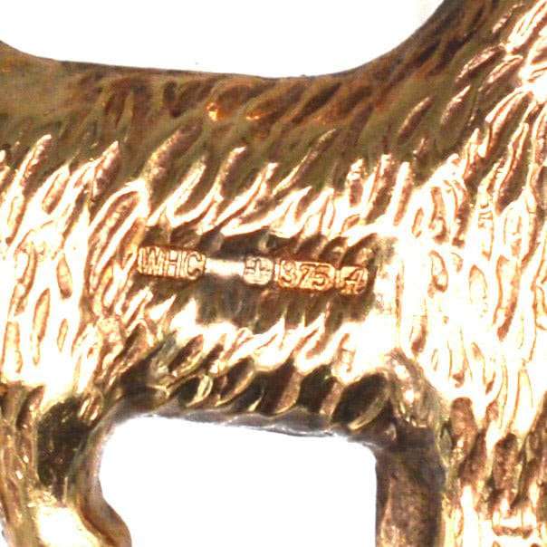 Close-up of a vintage 9ct gold Scottie dog charm pendant, detailing hallmark and texture.