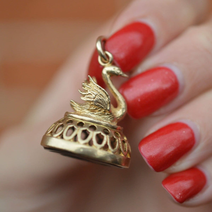 Vintage 9ct gold swan pendant held between fingers with red nail polish, showcasing intricate design and elegance.