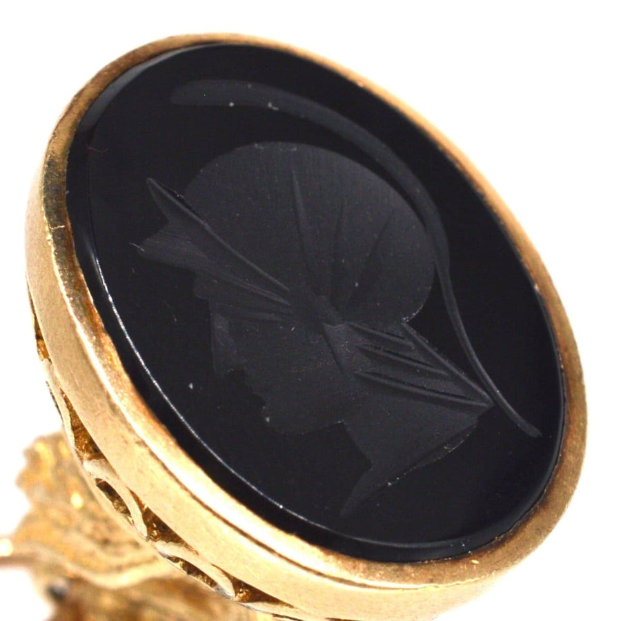 Close-up of a vintage gold pendant featuring an onyx seal engraved with the silhouette of Hermes, the Messenger of Gods.