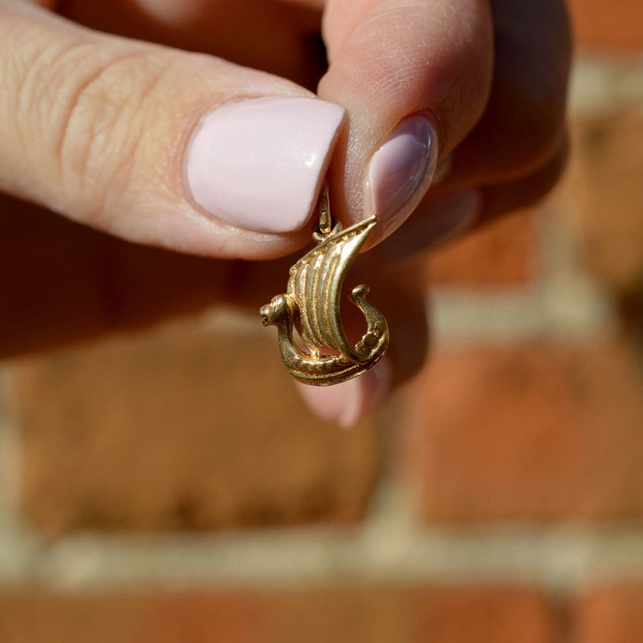 Hand holding a Vintage 9ct Gold Viking Ship Charm, showcasing its dragon head detail against a brick background.