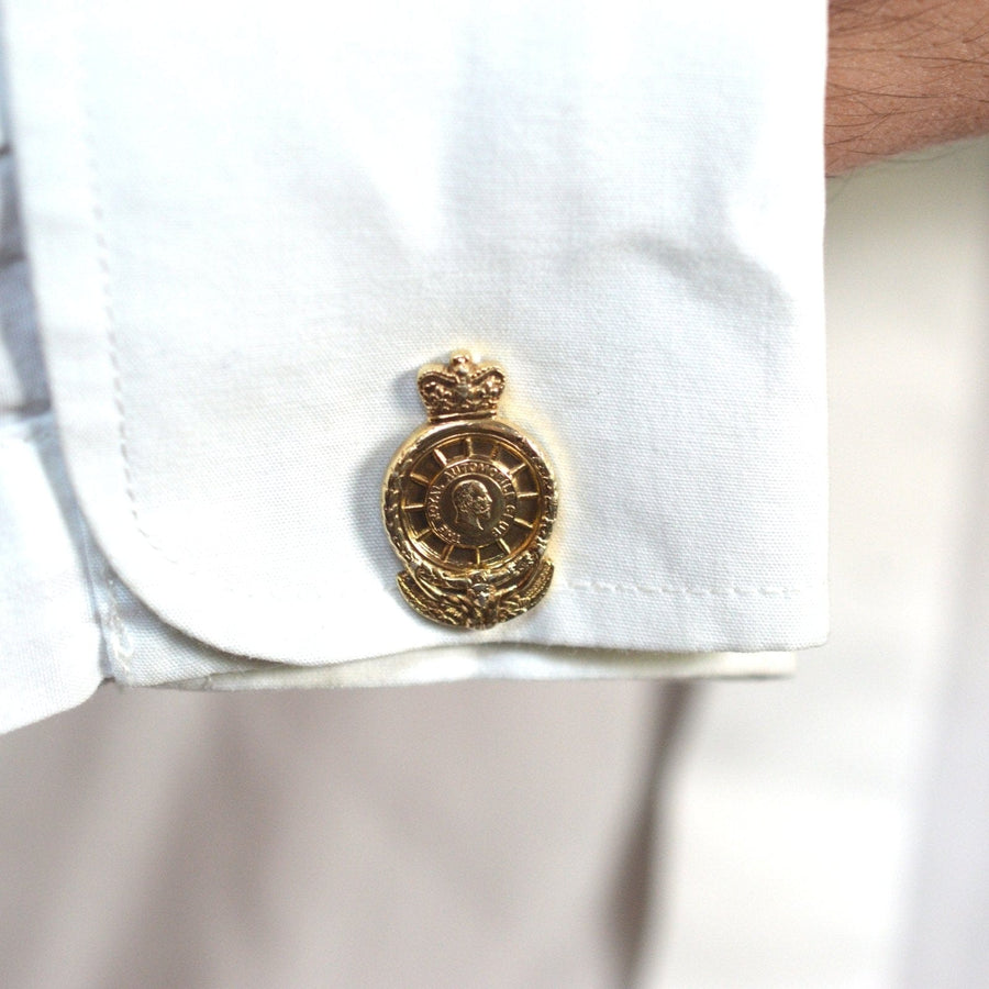 Close-up of vintage gold cufflink featuring the Royal Automobile Club logo on a white shirt cuff.