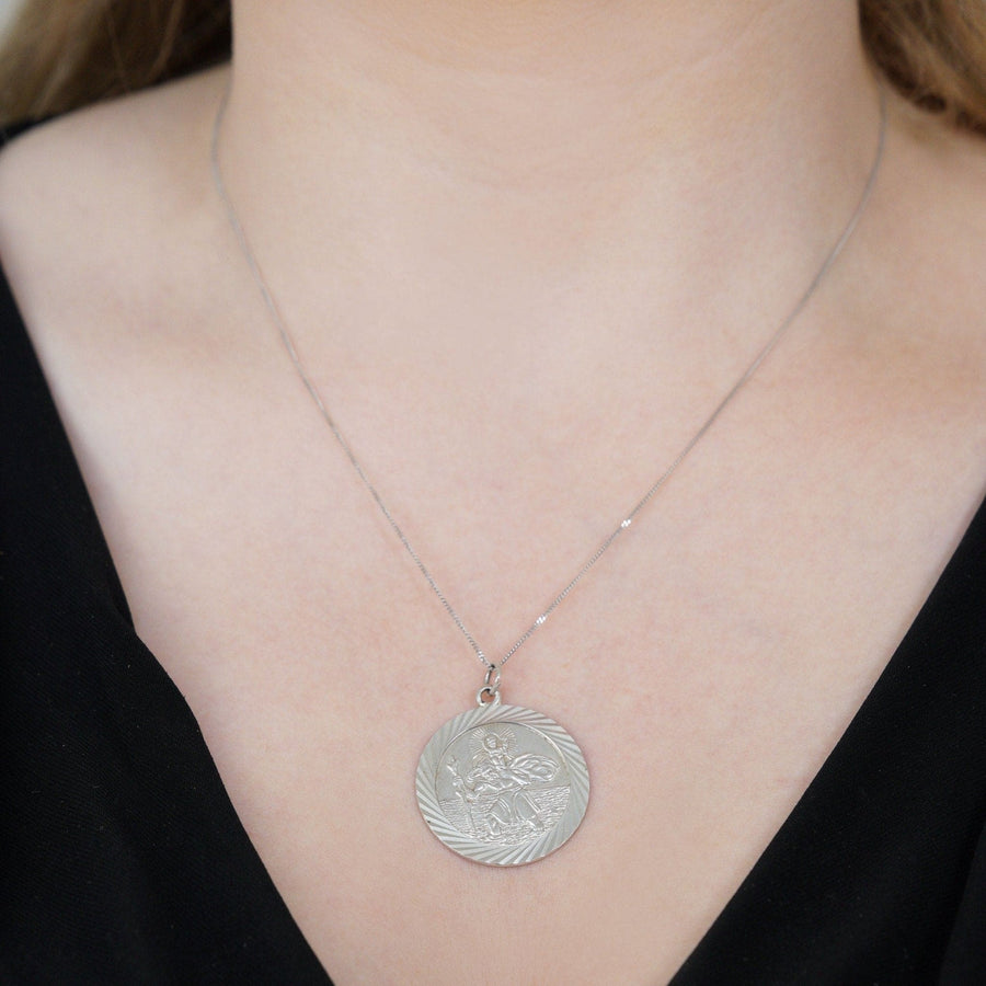 Vintage silver Saint Christopher round pendant worn on a delicate chain, symbolizing protection for travelers.